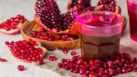 Segelas jus delima berwarna merah cerah dengan beberapa biji delima di sampingnya. Jus ini kaya antioksidan untuk menjaga kesehatan jantung dan menurunkan darah tinggi saat hamil.